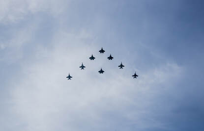 Helderblauwe lucht met van onderen te zien een hele strakke formatie van acht gevechtsvliegtuigen.