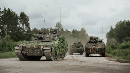 Drie gecamoufleerde CV90-infanteriegevechtsvoertuigen rijden op de fotograaf af.
