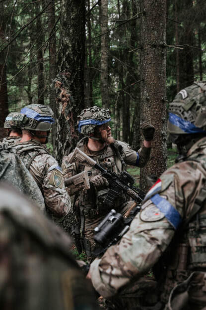 Vier militairen overleggen in bosrijke omgeving.