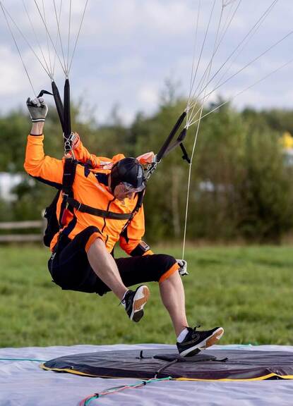 Een Nederlandse parachutist met oranje parachute landt op een kussen.