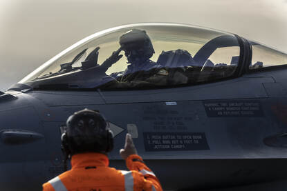 Een F-16 piloot salueert naar iemand van het grondpersoneel.