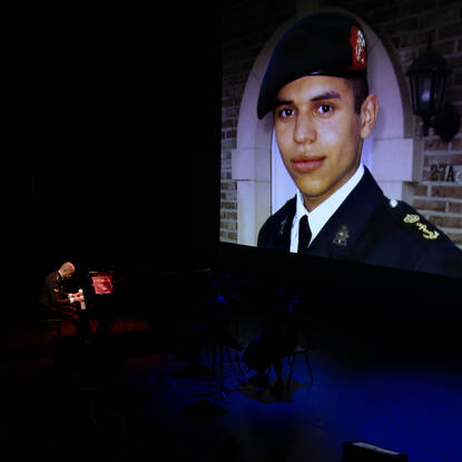 Nordin Maouili speelt op zijn piano. Op de achtergrond op een groot scherm een foto van vroeger, wanneer hij als jonge jongen zijn nette marinierspak met baret draagt.