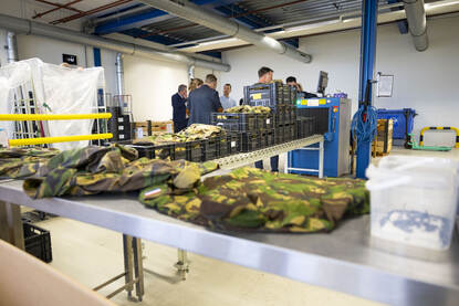 Militaire kleding ligt op een tafel. Erachter zijn dozen en mensen te zien.