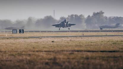 Een F-35 jachtvliegtuig stijgt op vanaf vliegbasis Leeuwarden. Op de voorgrond is gras.