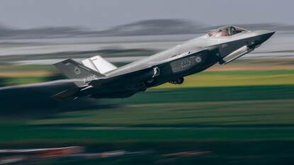 Links stijgt een F-35 in volle vaart op. Rechts rent een vlieger richting zijn gereedstaande kist.