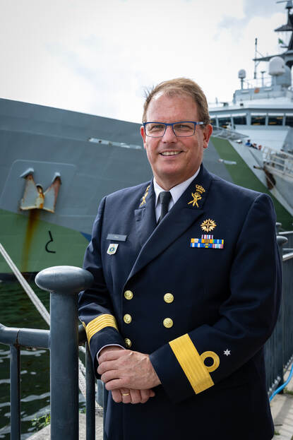 Commandeur Paul Flos voor een van de schepen die op de Thames bij Excel lag.