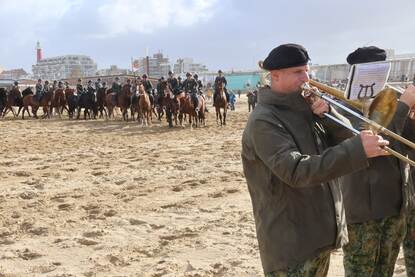 links: een fanfare speelt op het strand, op de achtergrond ruiters te paard. Rechts: Paarden rennen over het strand terwijl zand opstuift.