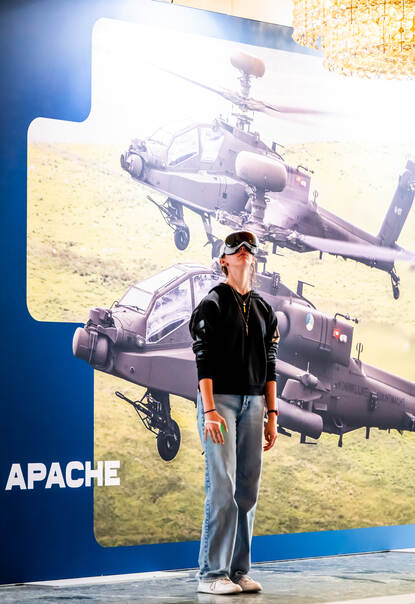 Jongen met VR-bril op kijkt rond. Achter hem een banner met daarop 2 Apaches.