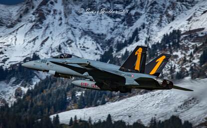 Links: een grijze straaljager in vlucht, met gele markeringen op de staart, vliegend boven besneeuwde bergen en dichte bossen. Rechts: in de verte landt een grijze straaljager, terwijl op de voorgrond een gevechtsvliegtuig klaar staat voor vertrek, met besneeuwde bergtoppen in beeld.