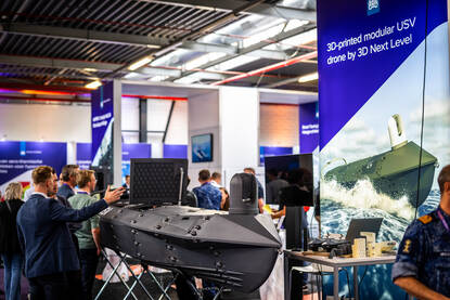 Links: Mannen in pakken staan rond een zwart bootje en een groot bord. Rechts: van bovenaf een inkijk in een grote zwarte boot.