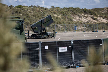 Links in beeld een NASAMS-lanceerinstallatie opgesteld op een parkeerplaats in de duinen. Rechts twee militairen met anti-drone-middelen.