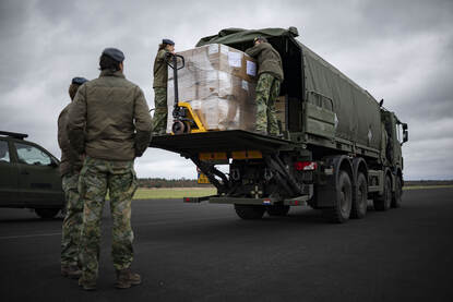 Op de linkerfoto geeft commandant Wesley een speech voor een groep toehoorders. Rechts laden militairen goederen in een vrachtwagen.