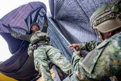 Op beide foto’s zijn militairen druk in de weer met grote zeildoeken om de Scania vrachtwagens te camoufleren.