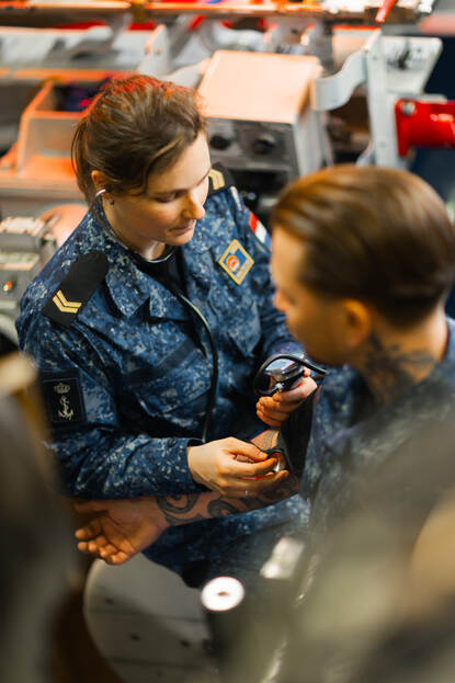 Korporaal en verpleegkundige Jeanine meet in de torpedokamer van de onderzeeboot de bloeddruk van een collega.