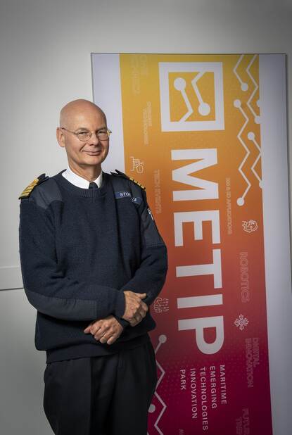 Militair staat voor banner en kijkt lachend in de camera.