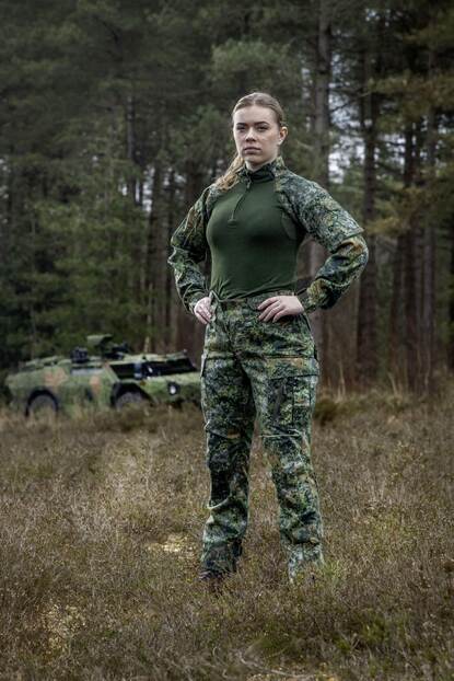 Een vrouwelijke militair toont het nieuwe tenue, op de achtergrond staat een militair voertuig.