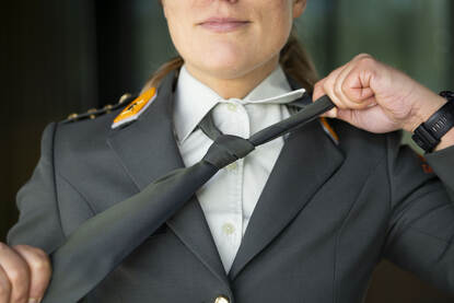 Een foto van dichtbij van een vrouwelijke landmachtmilitair die haar stropdas afdoet.