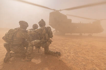 Een helikopter landt in de Iraakse woestijn. In het opstuivende zand knuilen 4 militairen voor de Chinook.