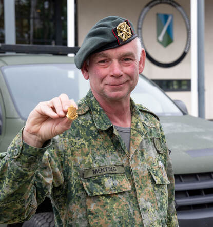 Adjudant Peter Menting houdt de ‘Air Defence’-speld vast voor zijn gezicht, staand voor het hoofdkwartier van het Defensie Grondgebonden Luchtverdedigingscommando in Vredepeel.