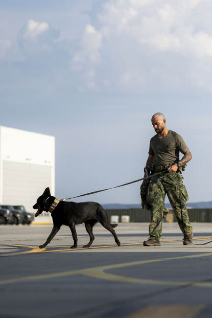 Een militair in luchtmachttenue loopt met een zwarte hond op een platform.