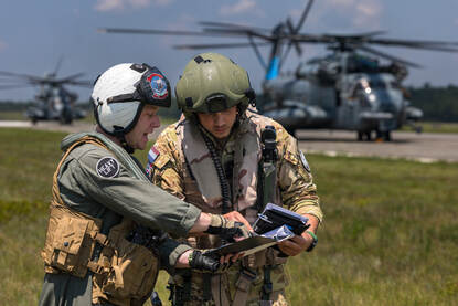 Twee personeelsleden in overleg met CH-53’s in de achtergrond.