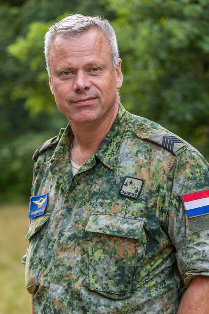 Portretfoto van sergeant-majoor Sander van der Haar, achter hem bomen.