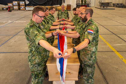 De acht militairen aan weerszijden van de kist vouwen de Nederlandse vlag tot een strak pakketje.