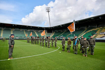 De vaandelwacht van de luchtmacht betreedt het veld vanuit een hoek van het stadion. De vaandeldrager in het midden, daaromheen militairen die een Colt C8-geweer vasthouden.