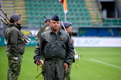 Luitenant-kolonel-vlieger van den Berg met een sabel in zijn hand. Hij staat opgesteld naast een pion, midden op het veld van het stadion.