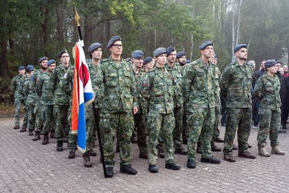 Militairen op een rij waarvan een aantal een vlag vasthouden.