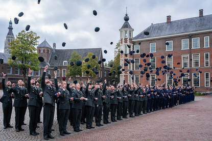 De in rijen opgestelde officieren gooien allen hun hoofddeksel in de lucht.