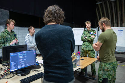 Militairen en burgers staan rondom een tafel met daarop computers.