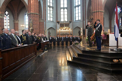 Een militair van de landmacht en marechaussee brengen een militaire groet vanaf het altaar aan de aanwezigen.