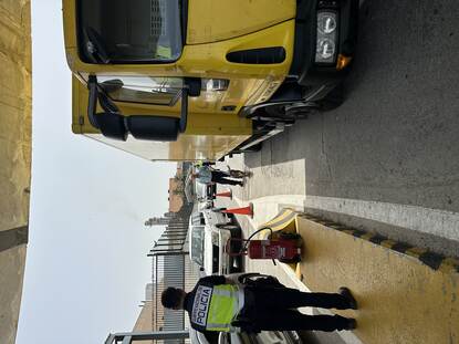 Opperwachtmeester Thijs loopt met Noa rond een gele vrachtwagen. Een Spaanse collega kijkt toe.