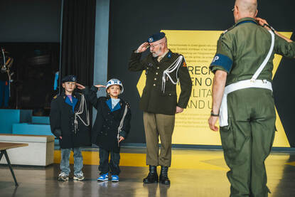 Marechaussee-veteraan salueert met twee kindjes naast zich die mee-salueren.