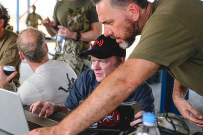 Medewerker van een dronefabrikant en militair kijken samen naar een laptopscherm.