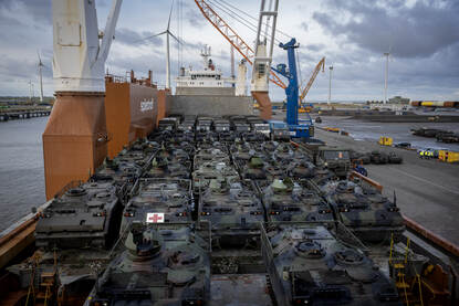 Tientallen pantservoertuigen en vrachtwagens van schuinboven gezien op het dek van een vrachtschip.