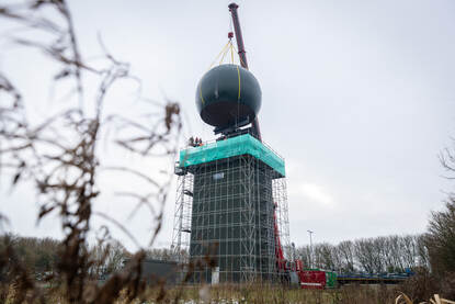 Radartoren met hijskraan die een bolvormige ‘dome’ over de radar plaats.