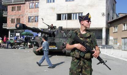 Militair met Gele Rijders muts met op achtergrond een M-109 houwitser.