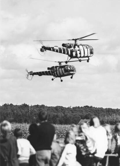 Twee Alouettes hangen boven de grond met publiek op de voorgrond.