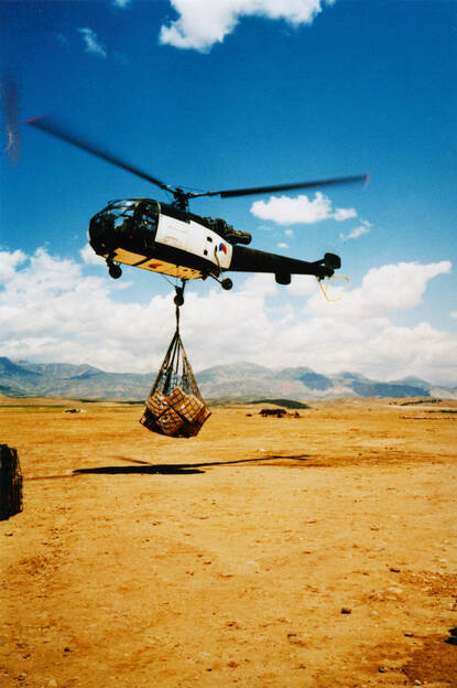 Alouette III met wit vlak tilt een net met hulpgoederen in de lucht.