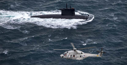 NH90 boven zee met Nederlandse onderzeeboot in het water.