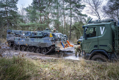 Berger legt trekband aan Scania vrachtwagen die diep in de modder vastzit.