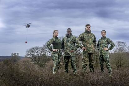 Militairen met het nieuwe uniform aan poseren voor de camera in het veld met op de achtergrond twee Chinook-helikopters.