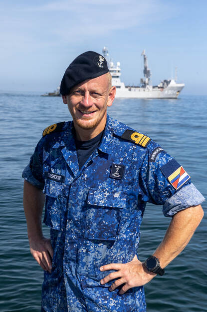 Portret van commandant Borsboom in blauw vlekkenpak met op de achtergrond de Pelikaan.