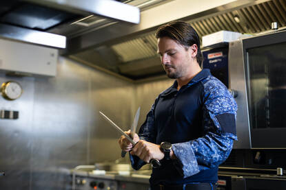 Vier foto’s met een vlootcollega die op een bootjes schiet, een gewonde marinier die medisch wordt geholpen en collega’s aan het werk in de kombuis.