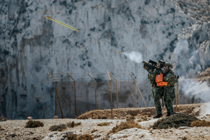 Een schutter schiet gesimuleerd met een Tracking Head Trainer op een F-16 van de Griekse luchtmacht op de NATO Missile Firing Installation (NAMFI). Foto ernaast: Een F-16 in de lucht.