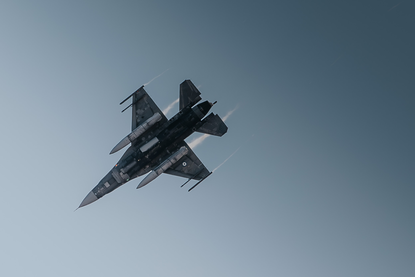 Een schutter schiet gesimuleerd met een Tracking Head Trainer op een F-16 van de Griekse luchtmacht op de NATO Missile Firing Installation (NAMFI). Foto ernaast: Een F-16 in de lucht.
