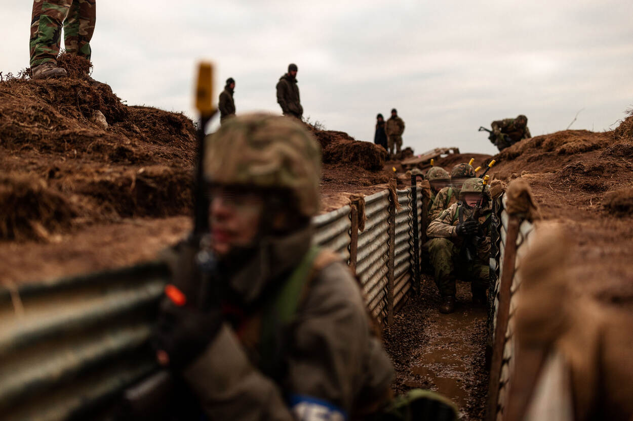 Geblurde Oekraïense militairen rennen door een loopgraaf. Instructeurs kijken toe.